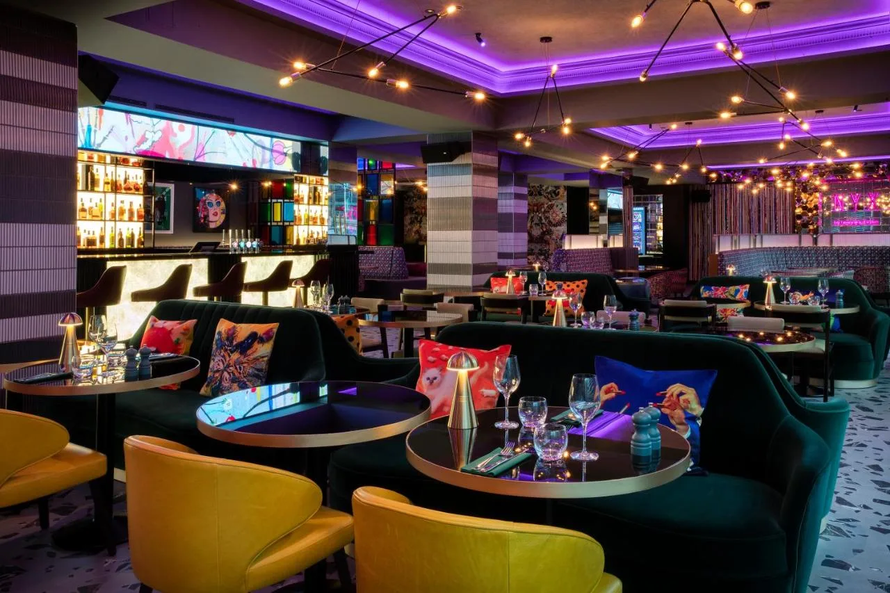 a restaurant with couches and tables and purple lighting at NYX Hotel London Holborn by Leonardo Hotels in London